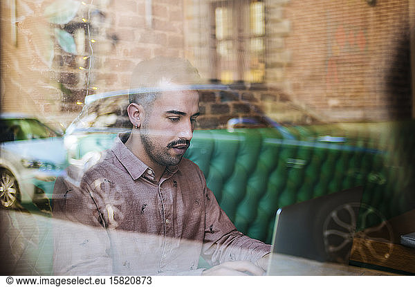 Man behind windowpane in a cafe using laptop