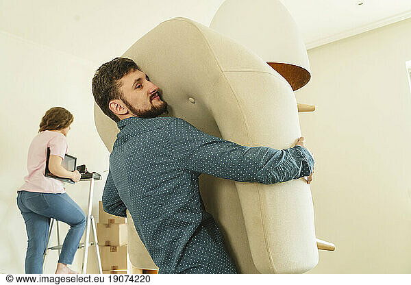 Man carrying armchair by girlfriend relocating in new house