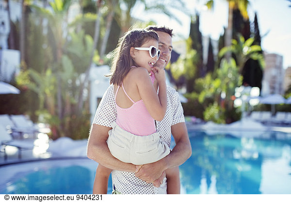 Man carrying his daughter by swimming pool