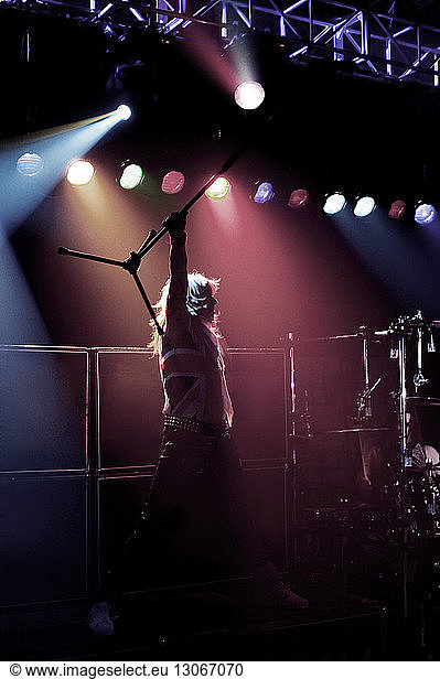 Man carrying microphone stand while standing on stage at concert