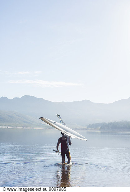 Man carrying rowing scull into lake