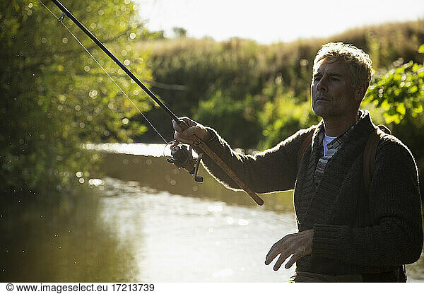Man casting fly fishing pole at sunny idyllic river