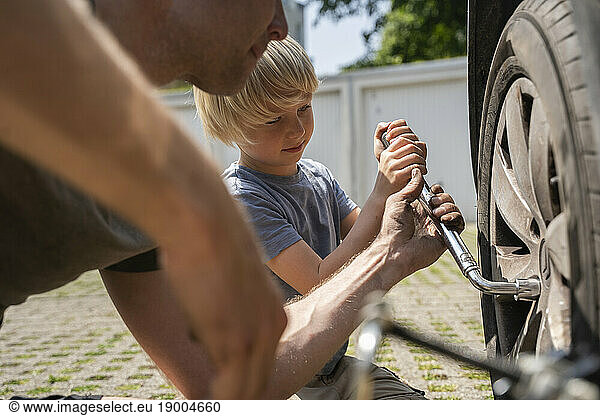 Man changing car tire with son in yard