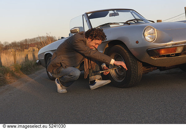 Man changing tyre of classic cabriolet car
