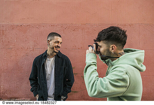 Man clicking photos of friend in front of wall