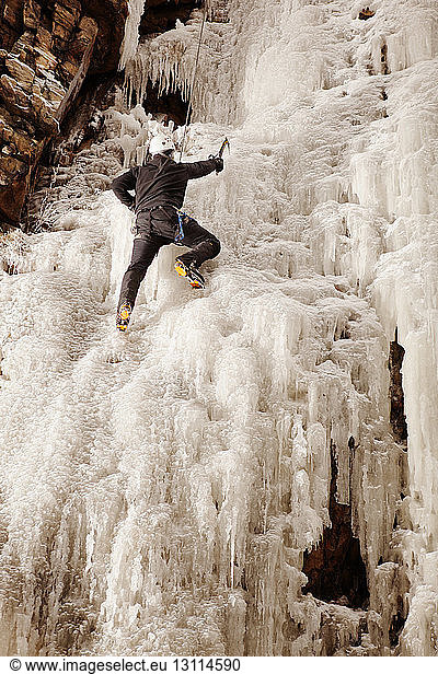 Man climbing frozen waterfall against rock formation