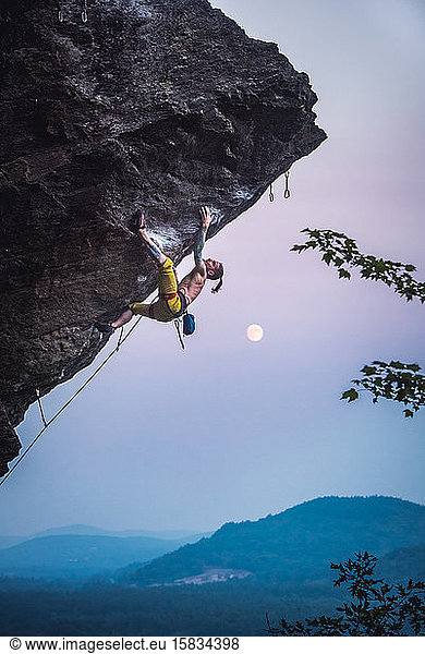 Man climbing overhanging sport climbing route with moon.