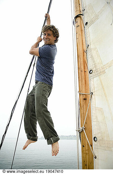 Man climbing rigging onboard sailboat  Casco Bay  Maine  New England.