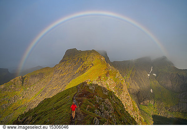 Man climbing towards a rainbow in the Lofoten Islands.