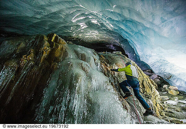 Man climbs frozen waterfall in ice cave below glacier