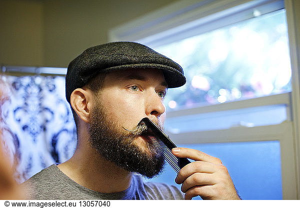 Man combing mustache while looking away at home