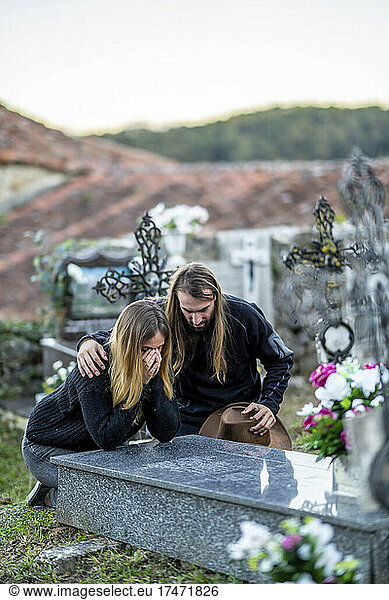 Man consoling woman at tombstone at cemetery