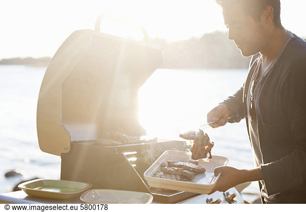 Man cooking beef near lake in bright sunlight
