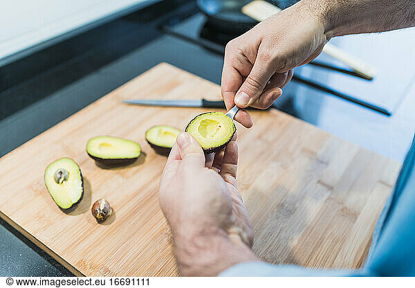 Man cooking in the kitchen in a denim shirt. An anonymous man is cooking avocados