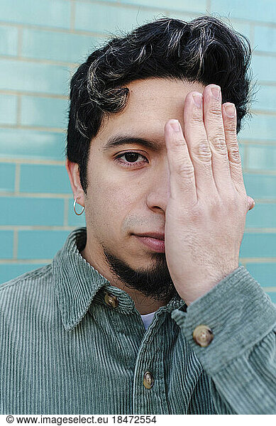 Man covering eye with hand in front of turquoise brick wall