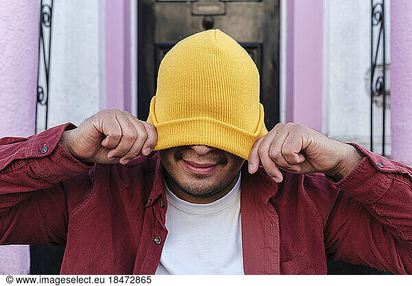 Man covering face with knit hat in front of door