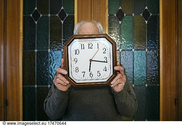 Man covering face with wall clock at home