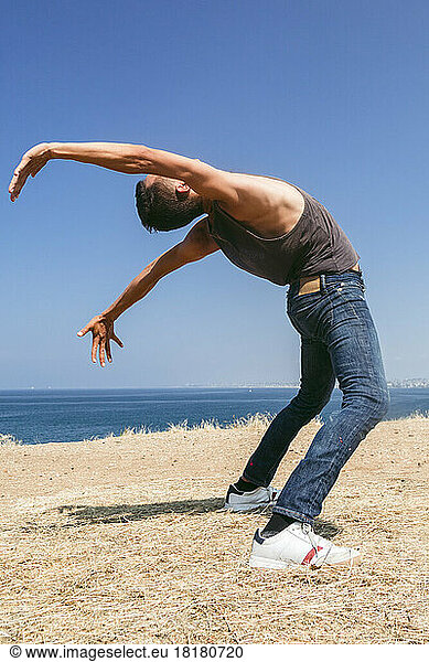Man dancing on field in front of sea on sunny day