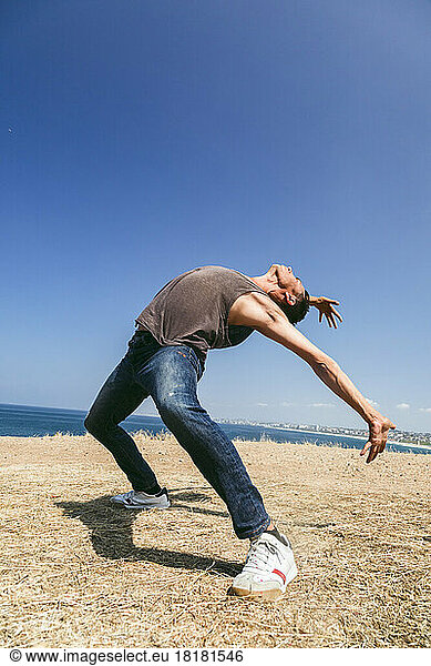 Man dancing on field in front of sea on sunny day