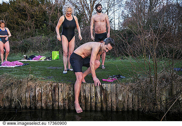 Man dipping feet in river with friends in background
