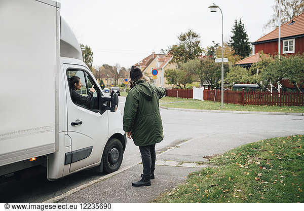 Man directing woman sitting in delivery van on street