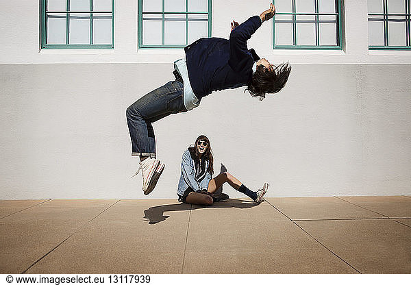 Man doing somersault while woman sitting against wall