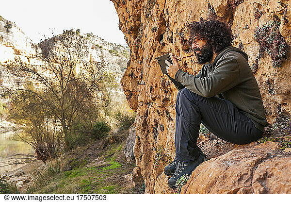 Man drawing in diary sitting on rocks near mountain