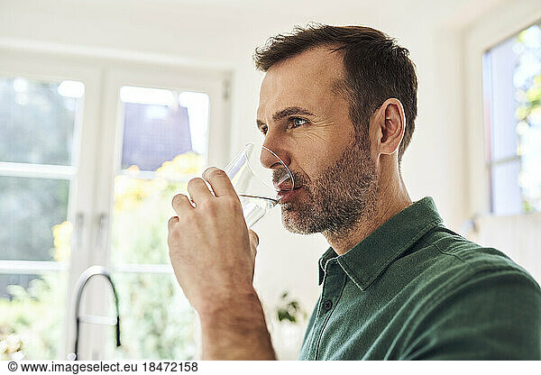 Man drinking glass of water standing in the kitchen