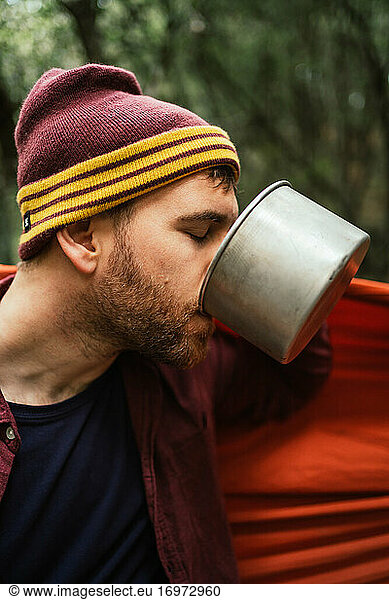 Man drinks hot beverage from a coffee pot in the forest