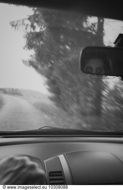 Man driving car while ghost watching him through rear view mirror