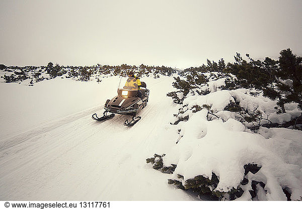 Man driving snowmobile on snowy field against sky