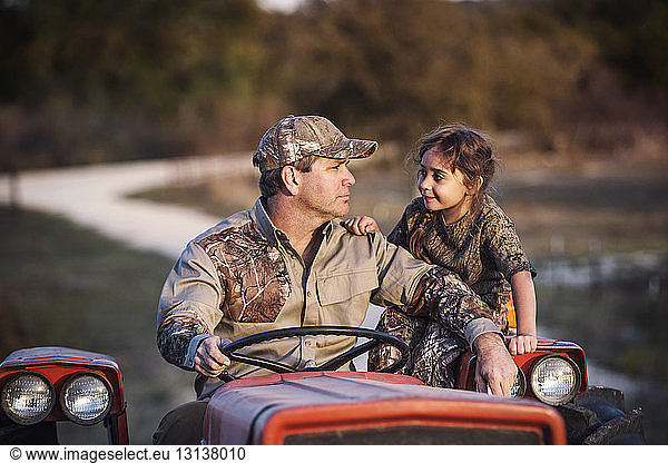 Man driving tractor while looking at daughter