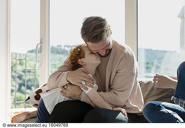 Man embracing cute preschool son while sitting by woman in living room at home