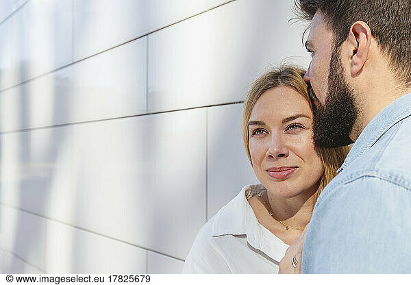 Man embracing girlfriend standing in front of wall