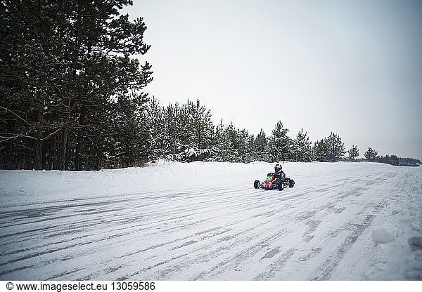 Man enjoying go-carts racing on snow covered field against sky