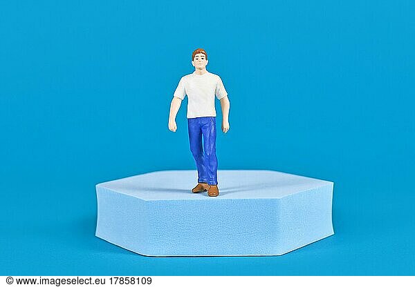 Man figure with shirt and jeans on pedestal in front of blue background