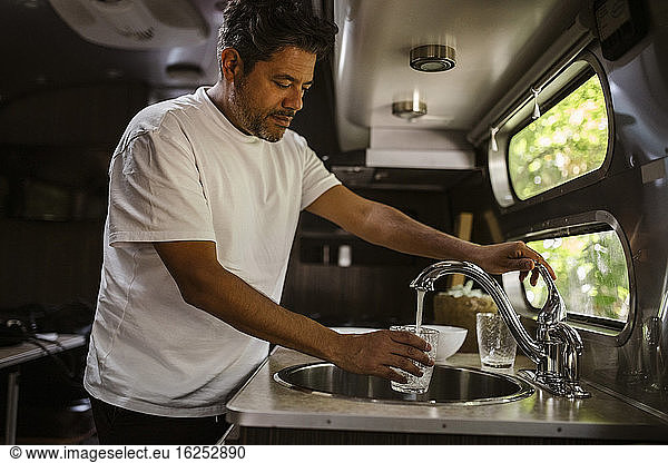 Man filling drinking water through faucet in camper trailer