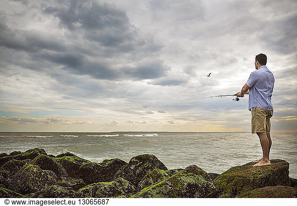 Man fishing while standing on rocks at beach