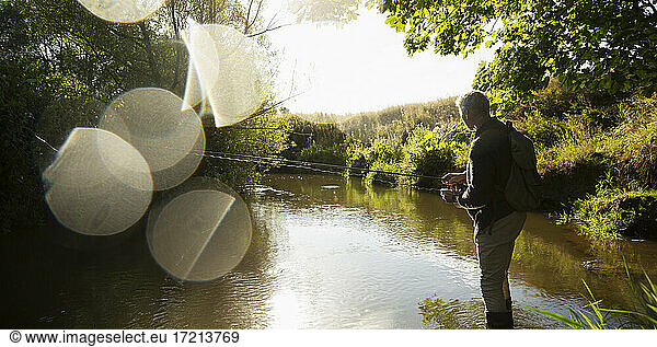 Man fly fishing at sunny idyllic river