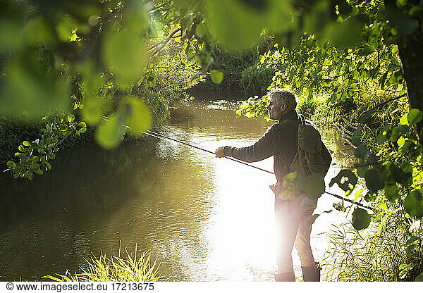 Man fly fishing at sunny idyllic summer riverbank