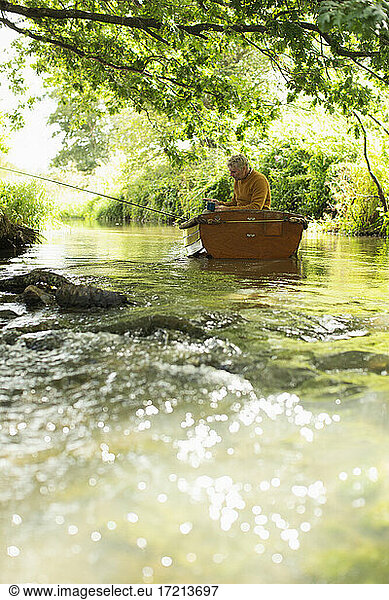 Man fly fishing in boat on idyllic river