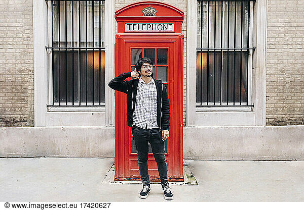 Man gesturing call me while standing in front of telephone booth