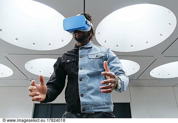 Man gesturing wearing virtual reality headset under illuminated ceiling