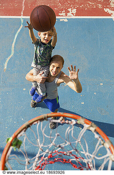 Man gesturing with son throwing basketball in hoop