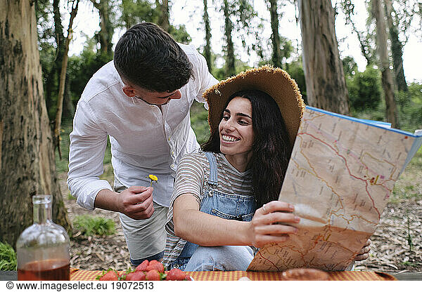 Man giving flower to woman holding map sitting in forest