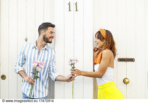 Man giving flowers to woman while leaning on white door