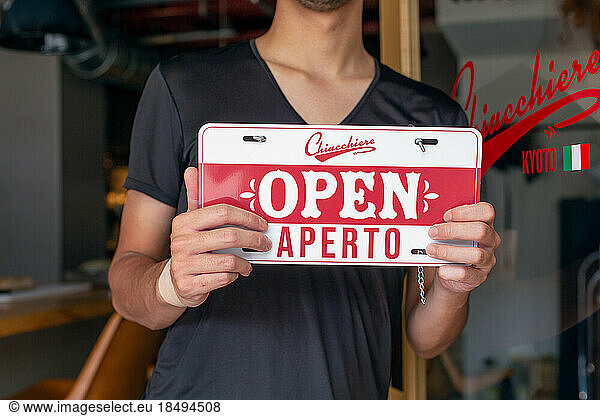 Man hanging up an Open sign on a restaurant door. Dual language  Italian and English.