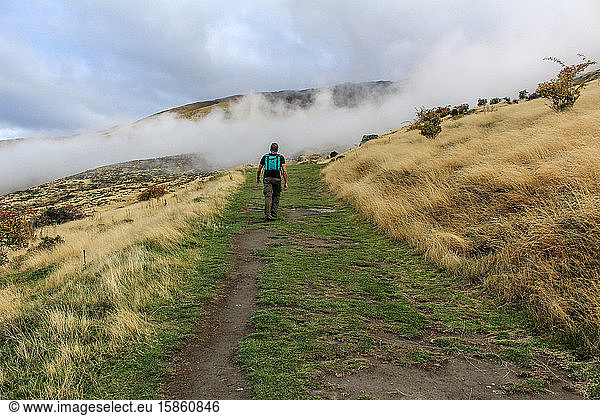 Man hiking into clouds covering mountain trail in New Zealand.
