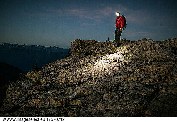 Man hiking on mountain with headlamp aid at night.