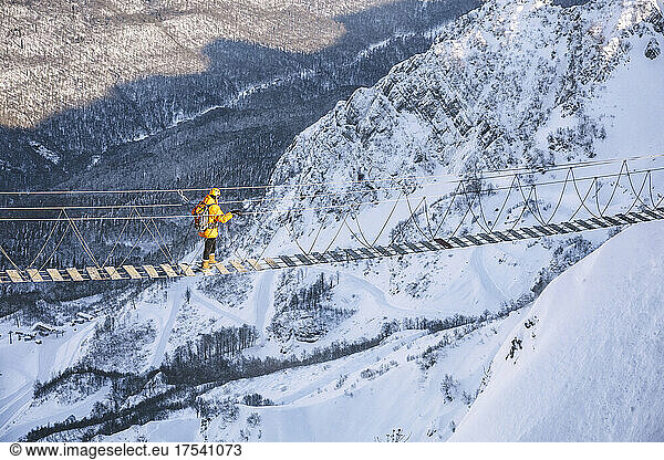 Man hiking over snowcapped mountain on rope bridge